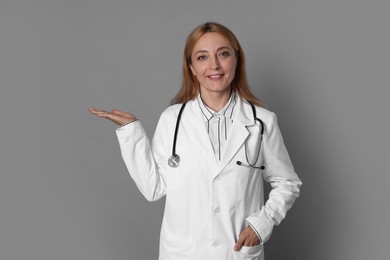 Doctor with stethoscope showing something on gray background