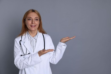 Doctor with stethoscope showing something on gray background, space for text