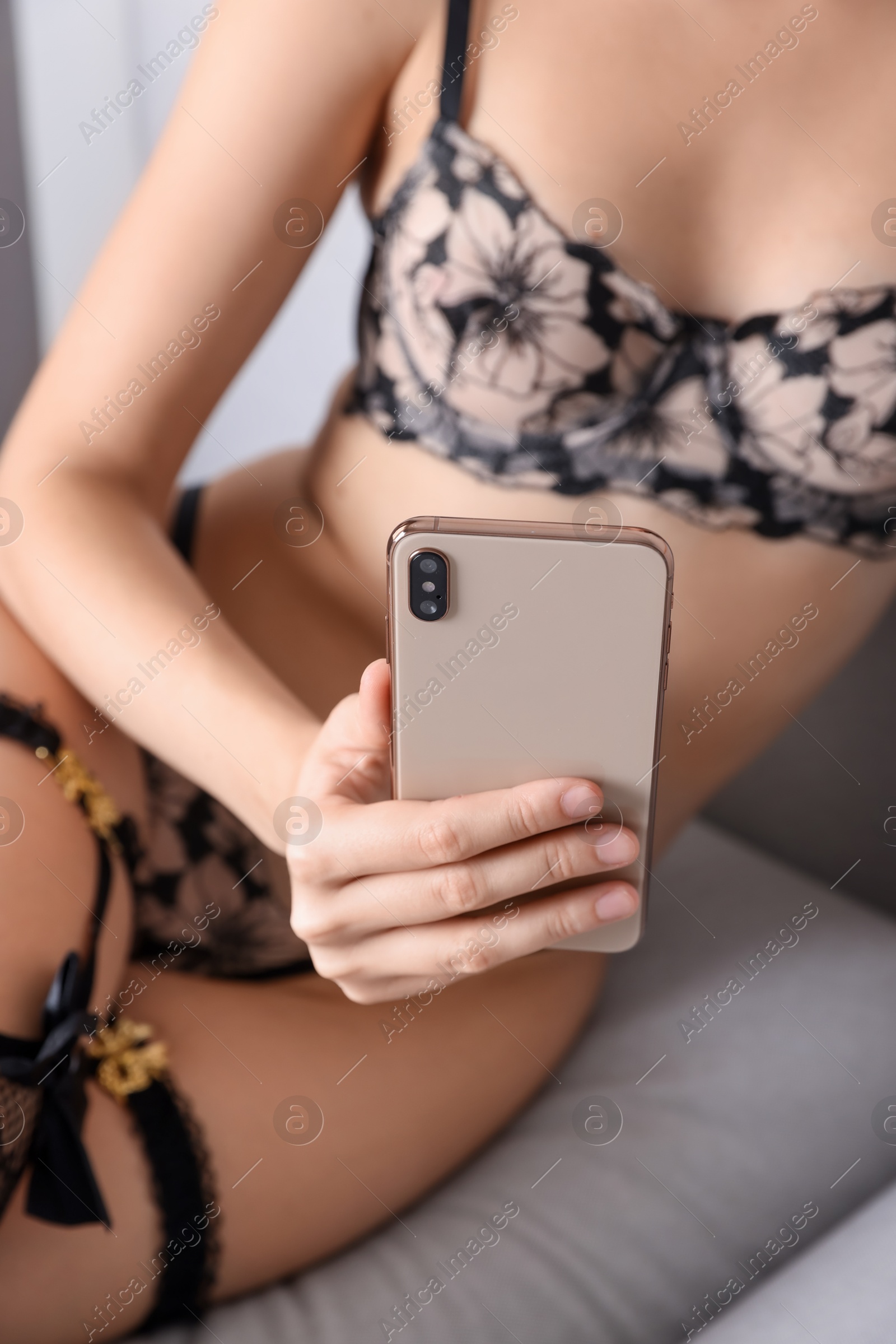 Photo of Prostitution. Webcam model in underwear working with smartphone on sofa indoors, closeup