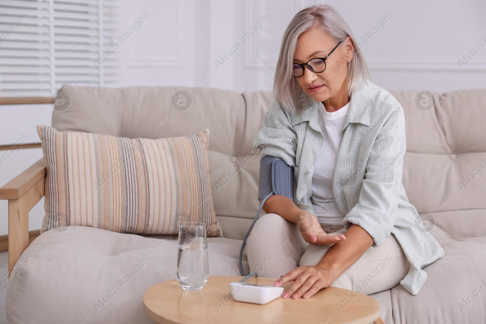 Photo of Woman measuring blood pressure on sofa indoors