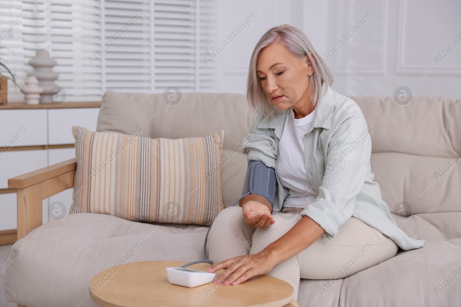 Photo of Woman measuring blood pressure on sofa indoors