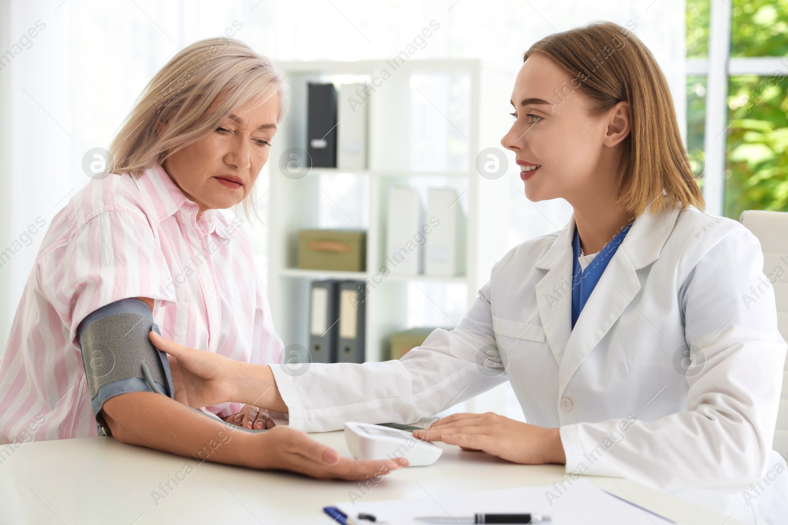 Photo of Doctor measuring patient's blood pressure at table in hospital