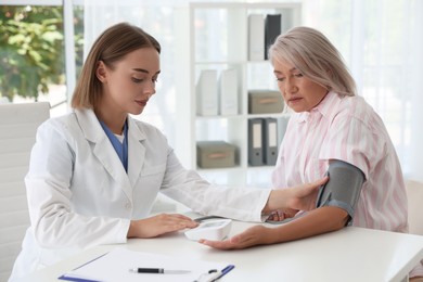 Photo of Doctor measuring patient's blood pressure at table in hospital