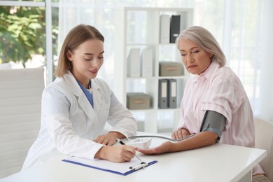 Doctor measuring patient's blood pressure at table in hospital