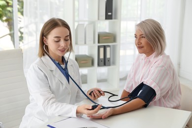 Photo of Doctor measuring patient's blood pressure at table in hospital