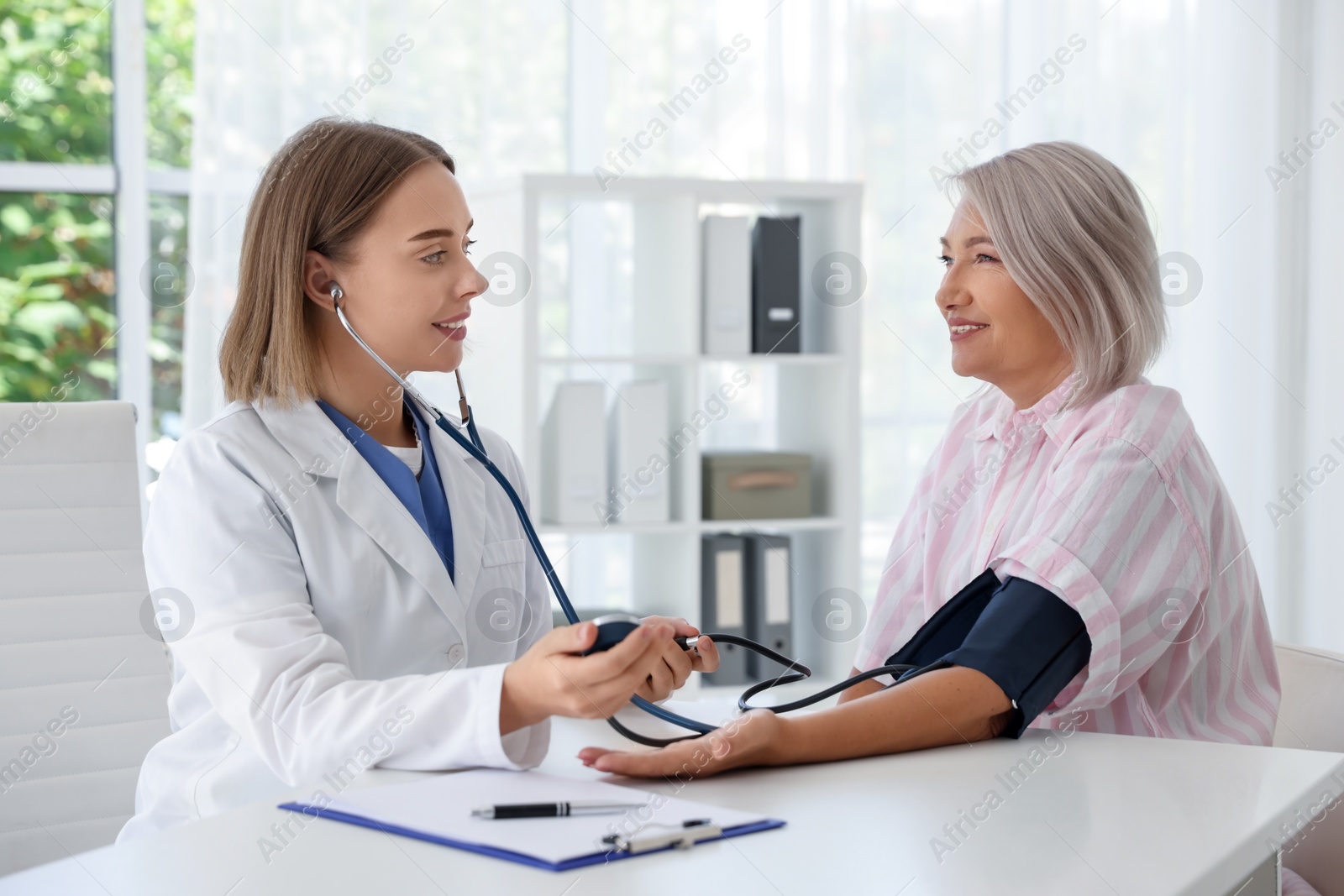 Photo of Doctor measuring patient's blood pressure at table in hospital