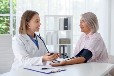 Doctor measuring patient's blood pressure at table in hospital