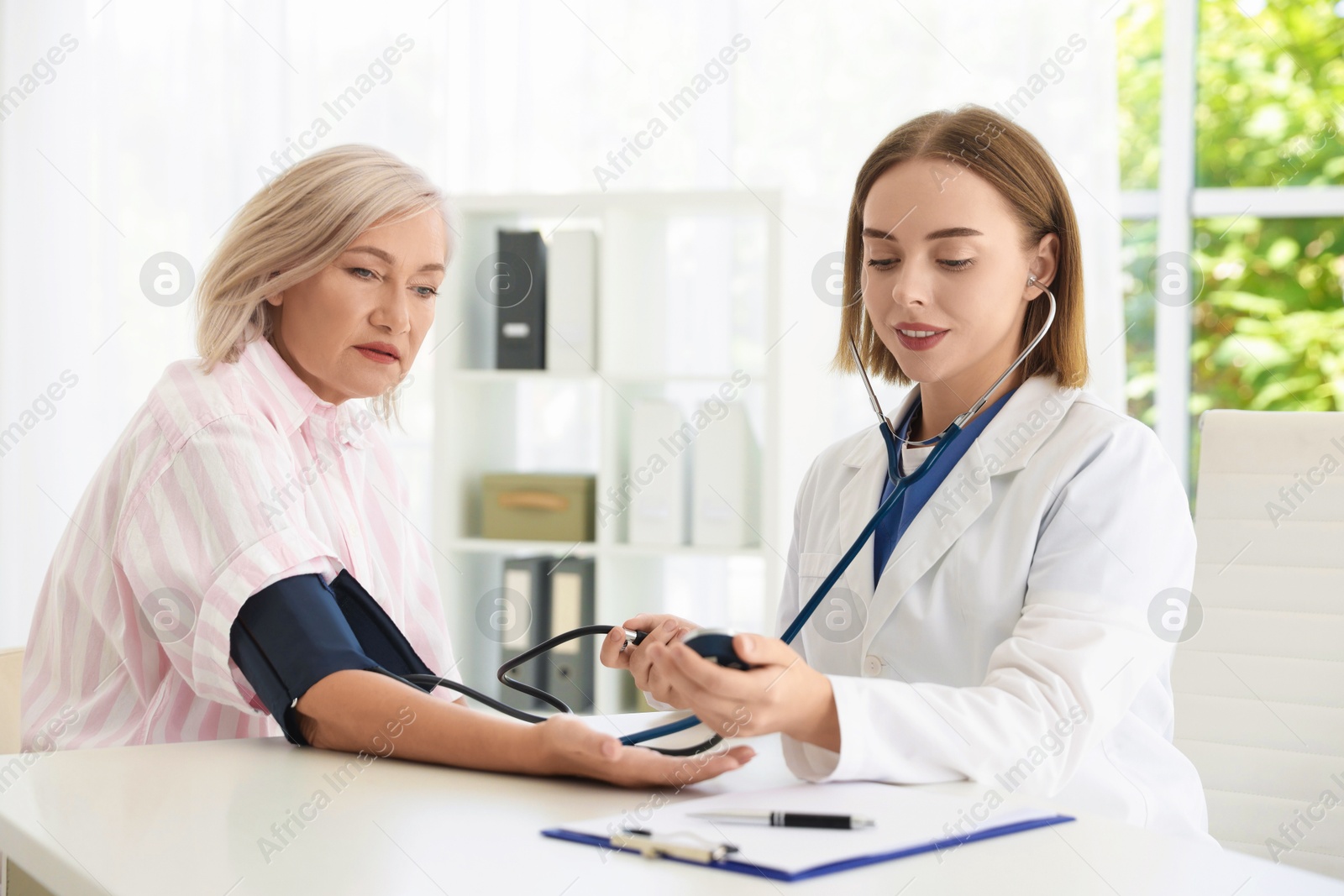 Photo of Doctor measuring patient's blood pressure at table in hospital