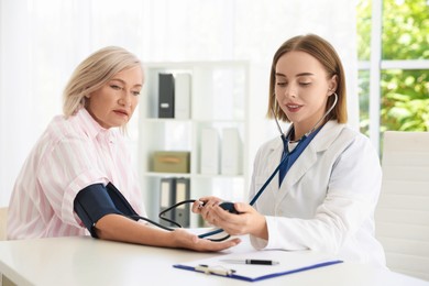 Doctor measuring patient's blood pressure at table in hospital