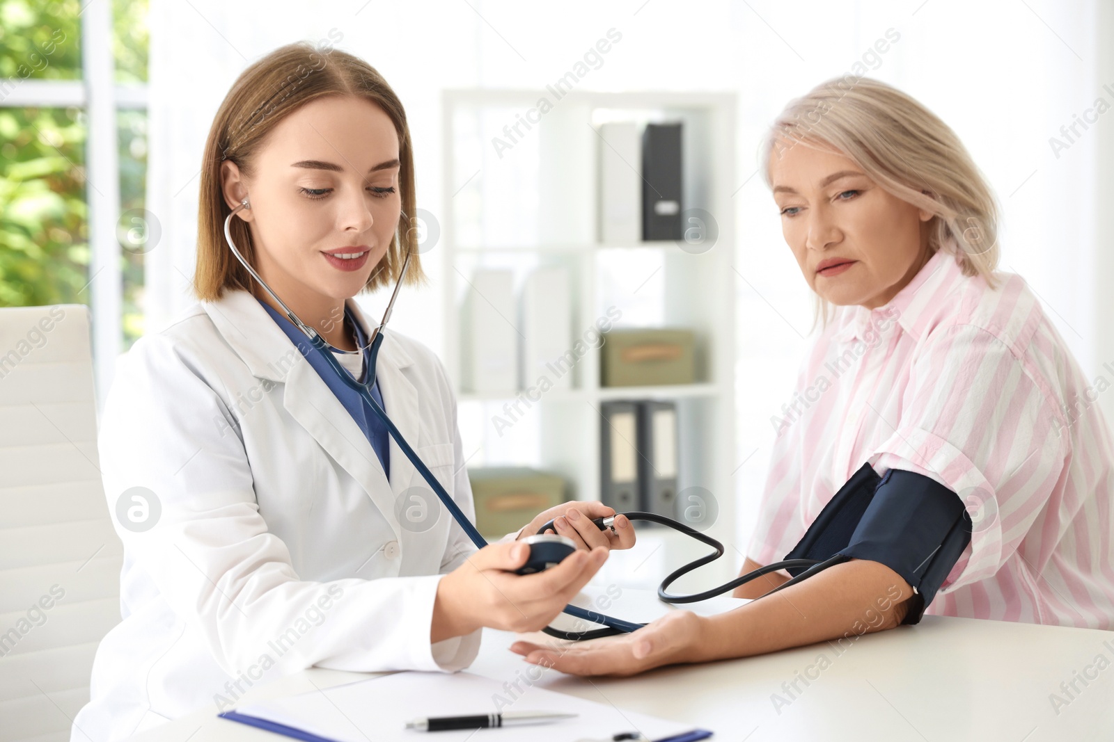 Photo of Doctor measuring patient's blood pressure at table in hospital