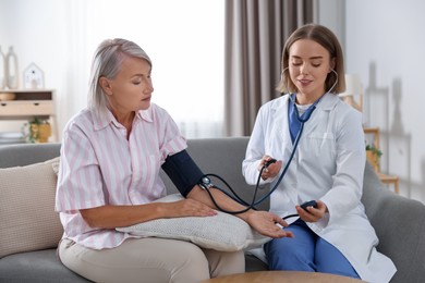 Doctor measuring patient's blood pressure on sofa indoors