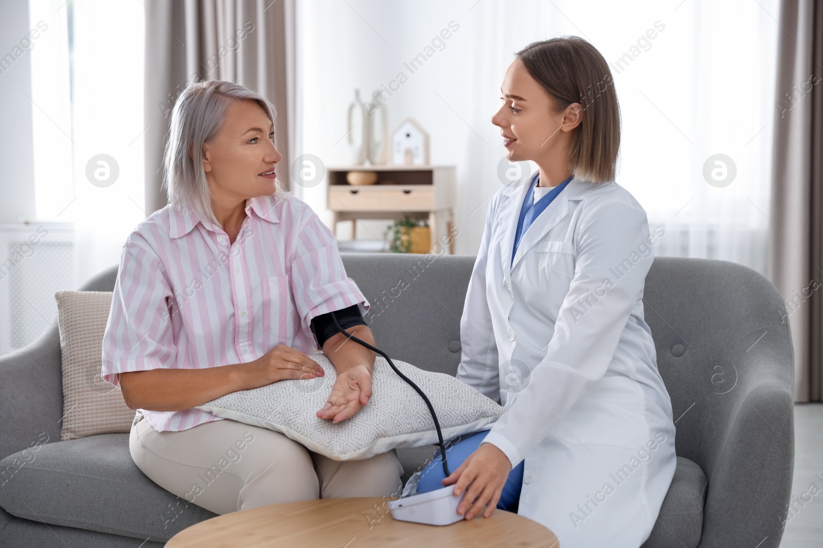 Photo of Doctor measuring patient's blood pressure on sofa indoors