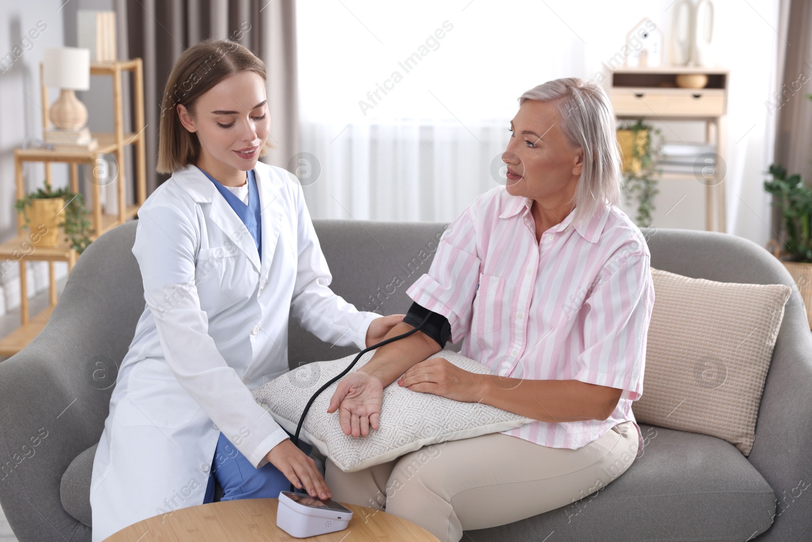 Photo of Doctor measuring patient's blood pressure on sofa indoors