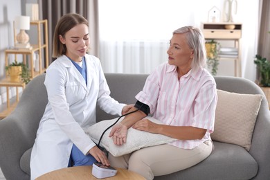 Doctor measuring patient's blood pressure on sofa indoors