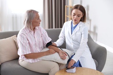 Doctor measuring patient's blood pressure on sofa indoors