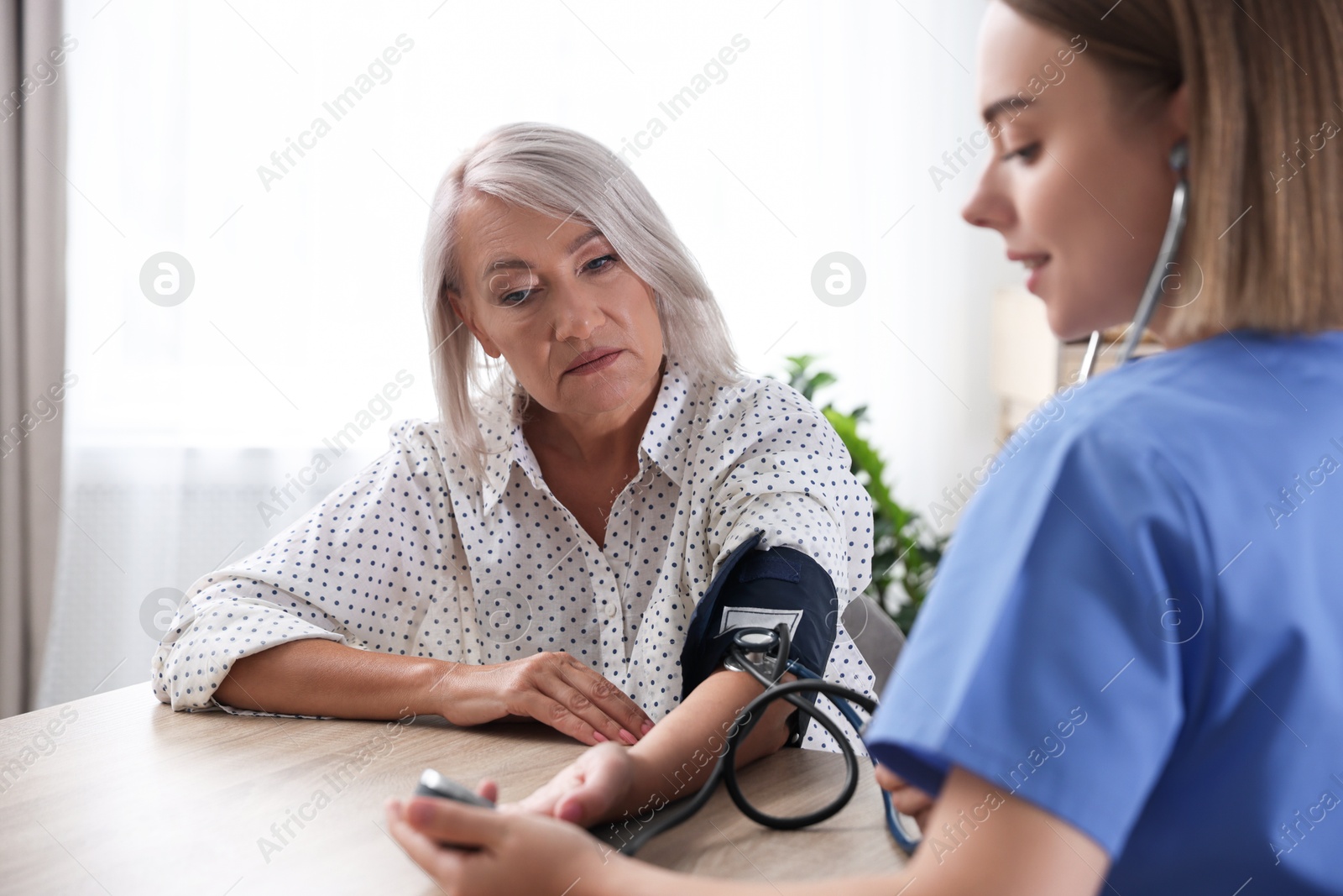 Photo of Healthcare worker measuring patient's blood pressure at wooden table indoors