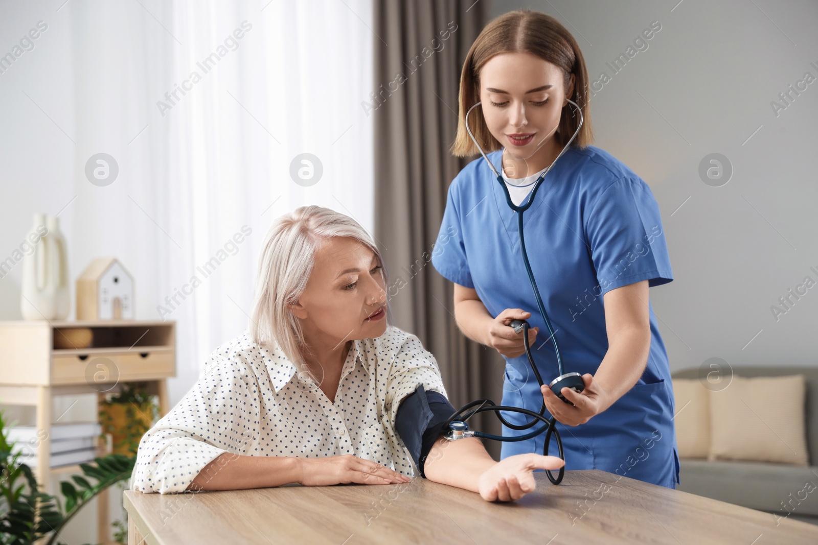 Photo of Healthcare worker measuring patient's blood pressure at wooden table indoors