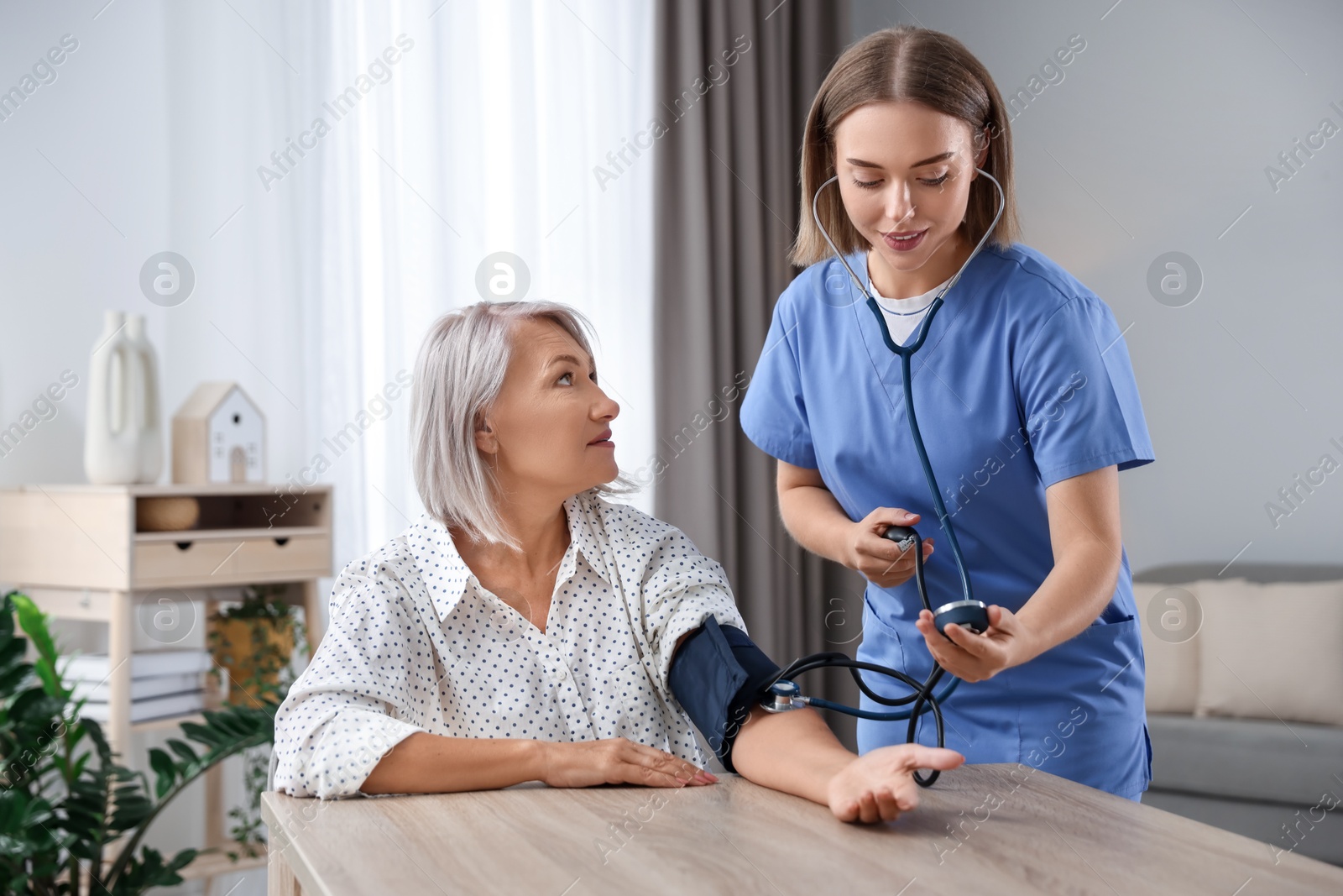 Photo of Healthcare worker measuring patient's blood pressure at wooden table indoors