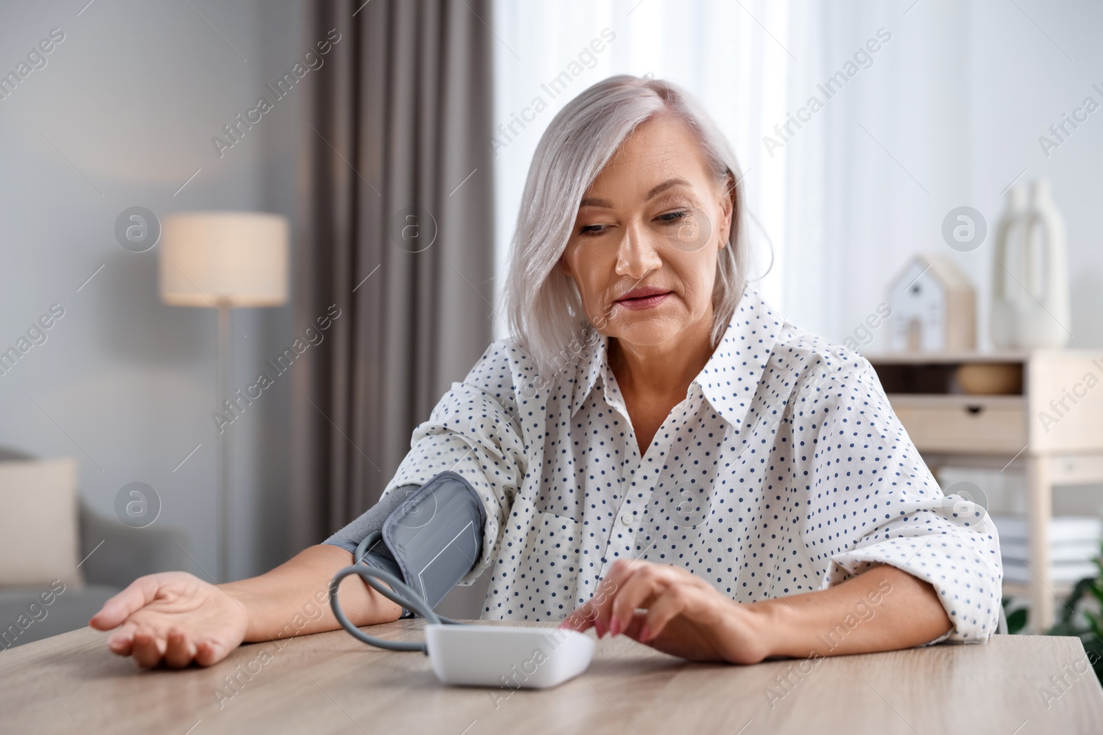 Photo of Woman measuring blood pressure at wooden table indoors