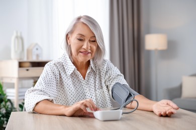 Photo of Woman measuring blood pressure at wooden table indoors