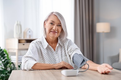 Photo of Woman measuring blood pressure at wooden table indoors