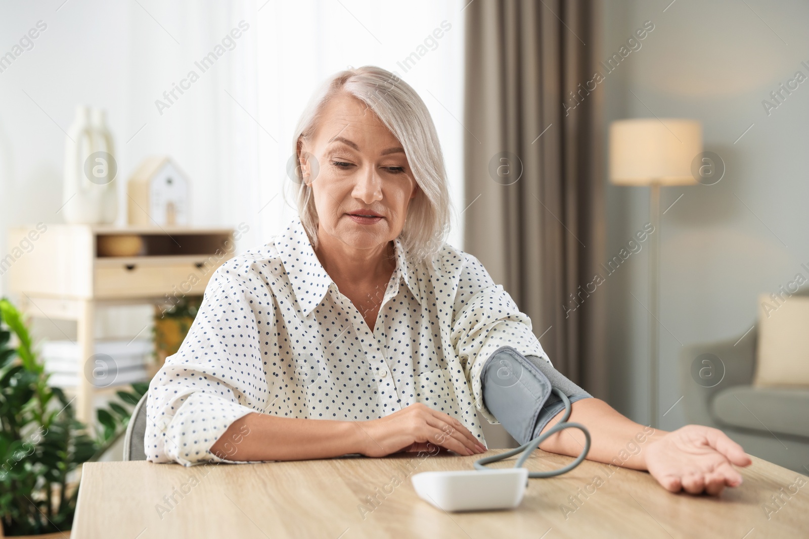 Photo of Woman measuring blood pressure at wooden table indoors