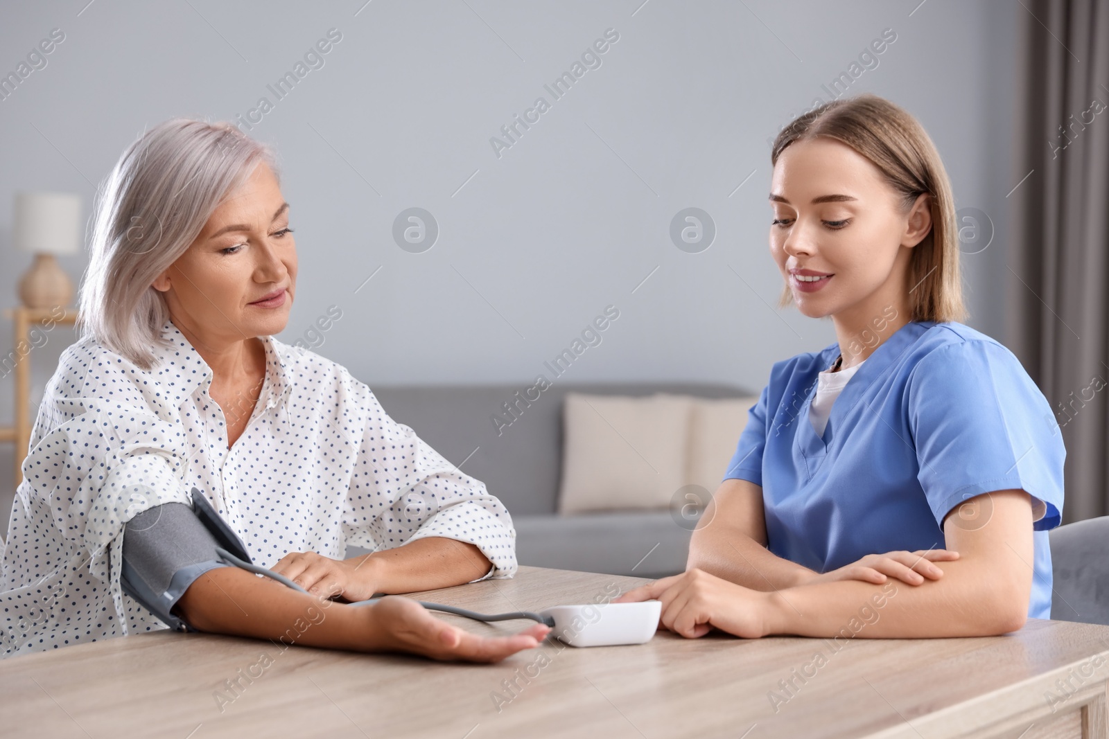 Photo of Healthcare worker measuring patient's blood pressure at wooden table indoors