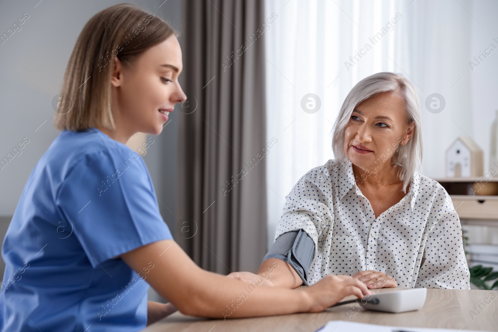 Photo of Healthcare worker measuring patient's blood pressure at wooden table indoors