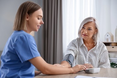 Healthcare worker measuring patient's blood pressure at wooden table indoors