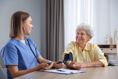 Photo of Healthcare worker measuring patient's blood pressure at wooden table indoors