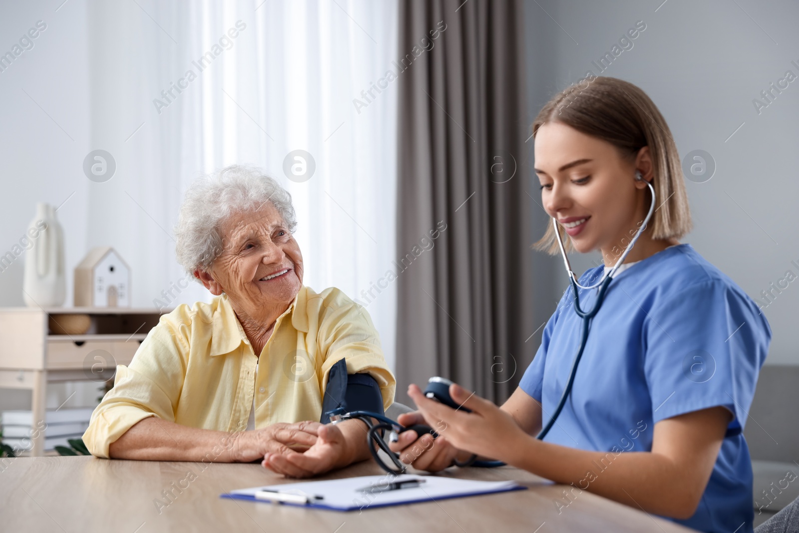 Photo of Healthcare worker measuring patient's blood pressure at wooden table indoors