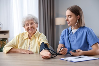 Photo of Healthcare worker measuring patient's blood pressure at wooden table indoors