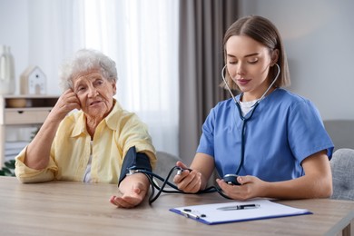 Healthcare worker measuring patient's blood pressure at wooden table indoors