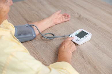 Photo of Senior woman measuring blood pressure at wooden table indoors, closeup