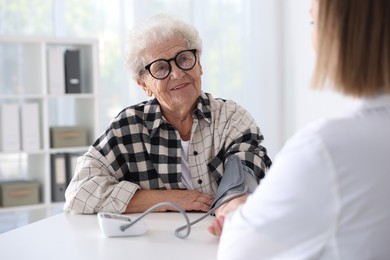 Doctor measuring patient's blood pressure at table in hospital