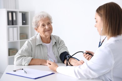 Photo of Doctor measuring patient's blood pressure at table in hospital