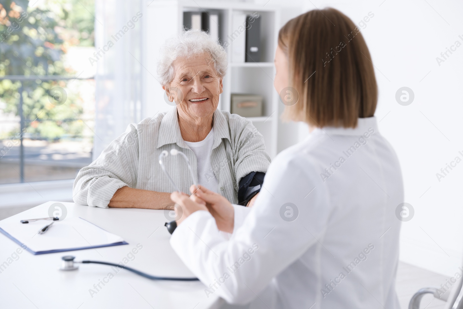 Photo of Doctor measuring patient's blood pressure at table in hospital