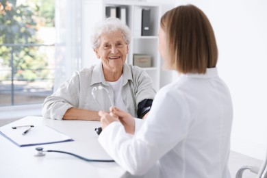 Doctor measuring patient's blood pressure at table in hospital