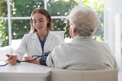 Doctor measuring patient's blood pressure at table in hospital