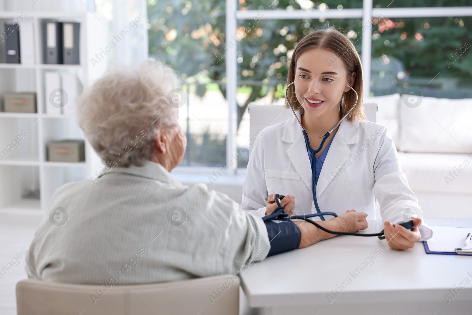 Photo of Doctor measuring patient's blood pressure at table in hospital