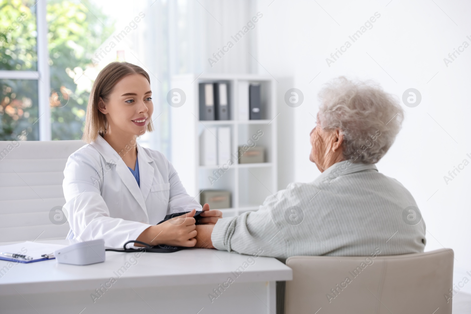 Photo of Doctor measuring patient's blood pressure at table in hospital