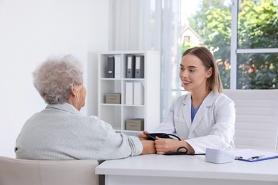 Photo of Doctor measuring patient's blood pressure at table in hospital