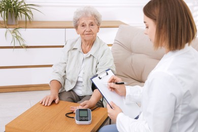 Senior woman measuring blood pressure while doctor taking notes indoors