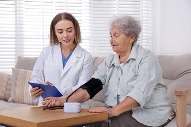 Senior woman measuring blood pressure while doctor taking notes indoors