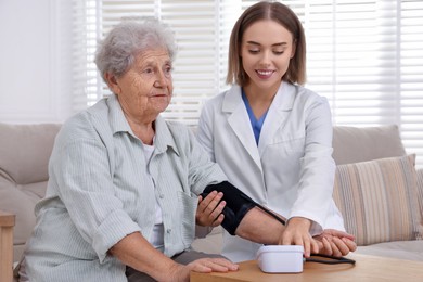 Doctor measuring patient's blood pressure at wooden table indoors