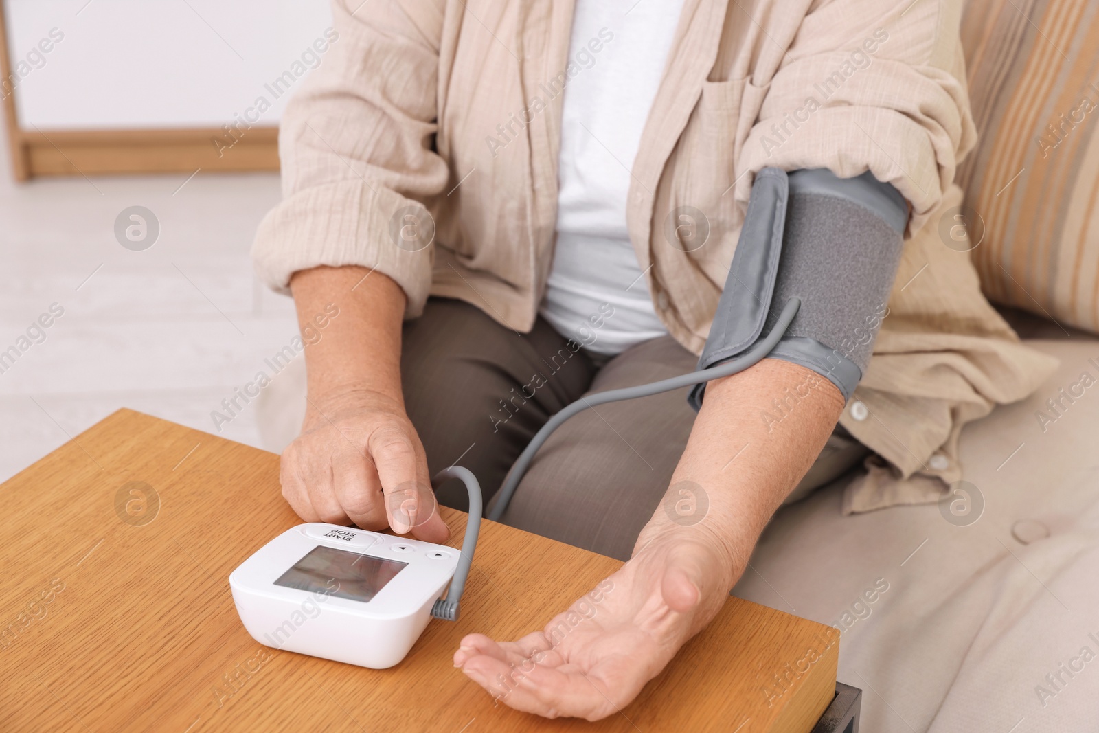 Photo of Senior woman measuring blood pressure at wooden table indoors, closeup