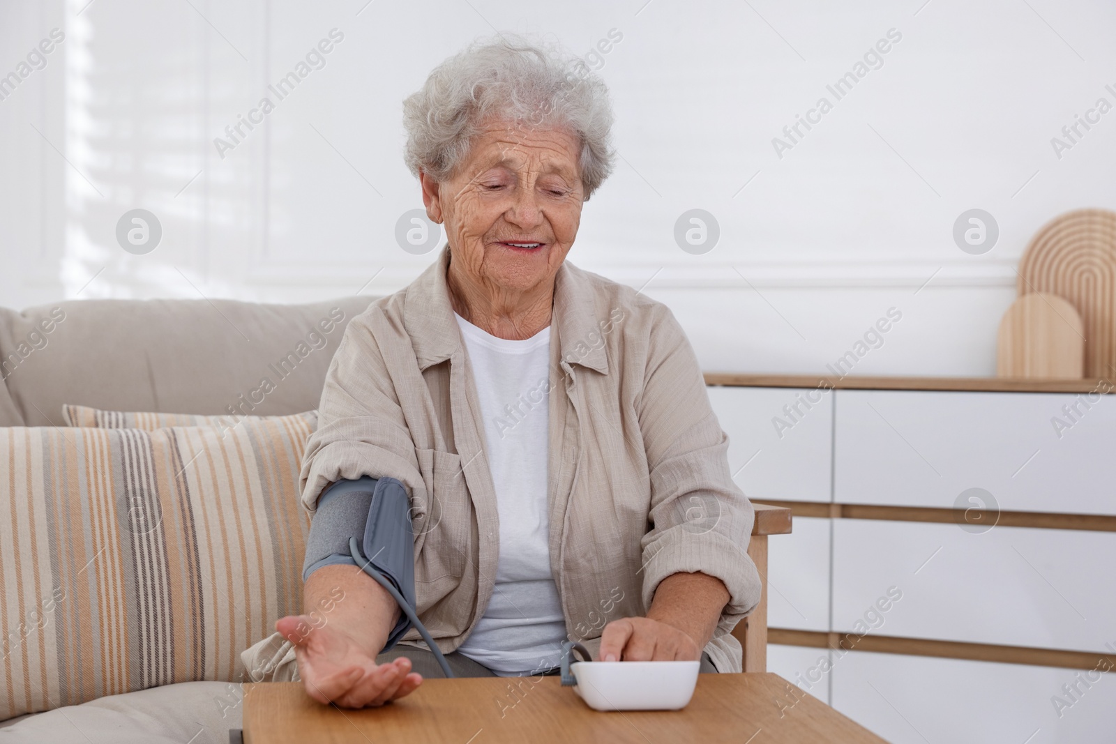 Photo of Senior woman measuring blood pressure at wooden table indoors