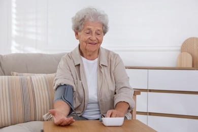 Senior woman measuring blood pressure at wooden table indoors