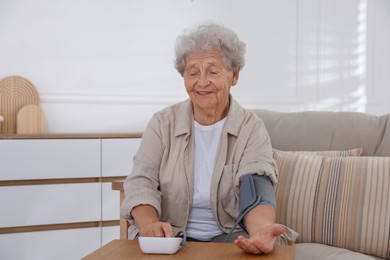 Photo of Senior woman measuring blood pressure at wooden table indoors