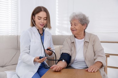 Photo of Doctor measuring patient's blood pressure at wooden table indoors